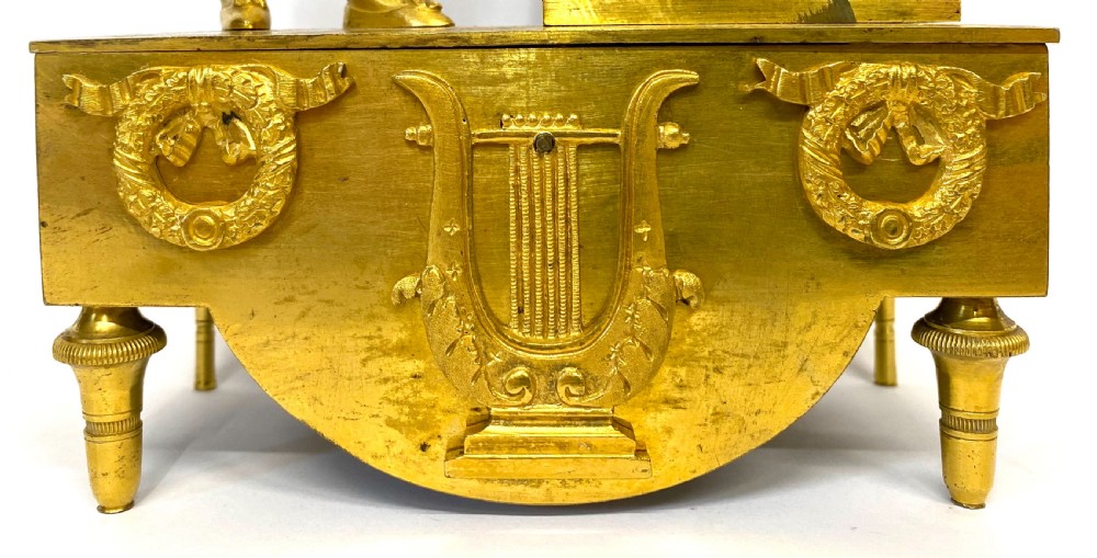An antique gilt bronze mantel clock featuring a standing figure of a flute player beside a circular white dial topped with a music stand. View VI