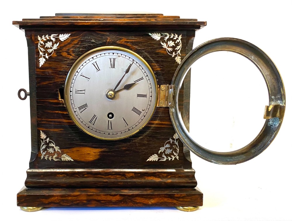 An antique coromandel wood mantel clock featuring mother-of-pearl corner inlays, a round brass bezel, and a silvered dial with Roman numerals. View III