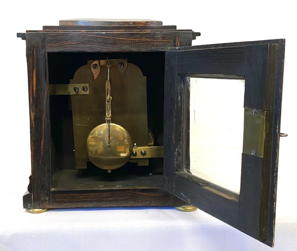 An antique coromandel wood mantel clock featuring mother-of-pearl corner inlays, a round brass bezel, and a silvered dial with Roman numerals. View X