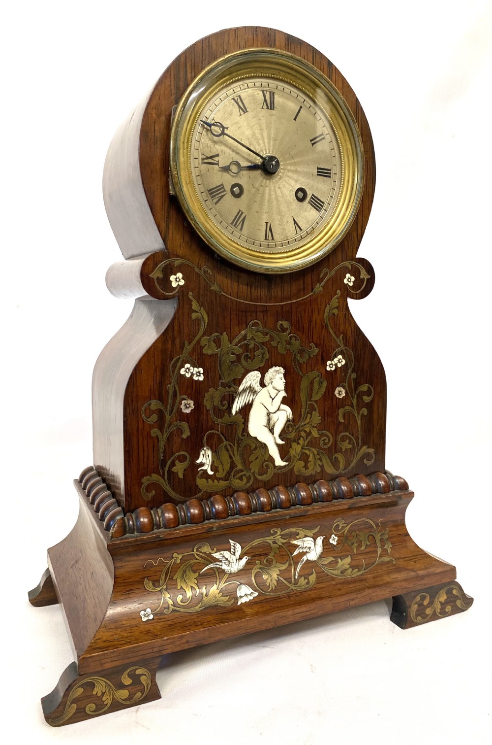 An antique French rosewood mantel clock featuring detailed brass foliage marquetry, bone cherub inlay, and a circular Roman numeral dial. View II