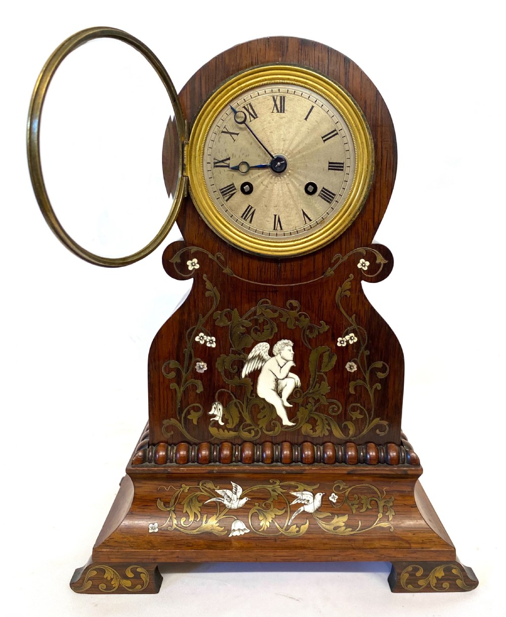 An antique French rosewood mantel clock featuring detailed brass foliage marquetry, bone cherub inlay, and a circular Roman numeral dial. View III