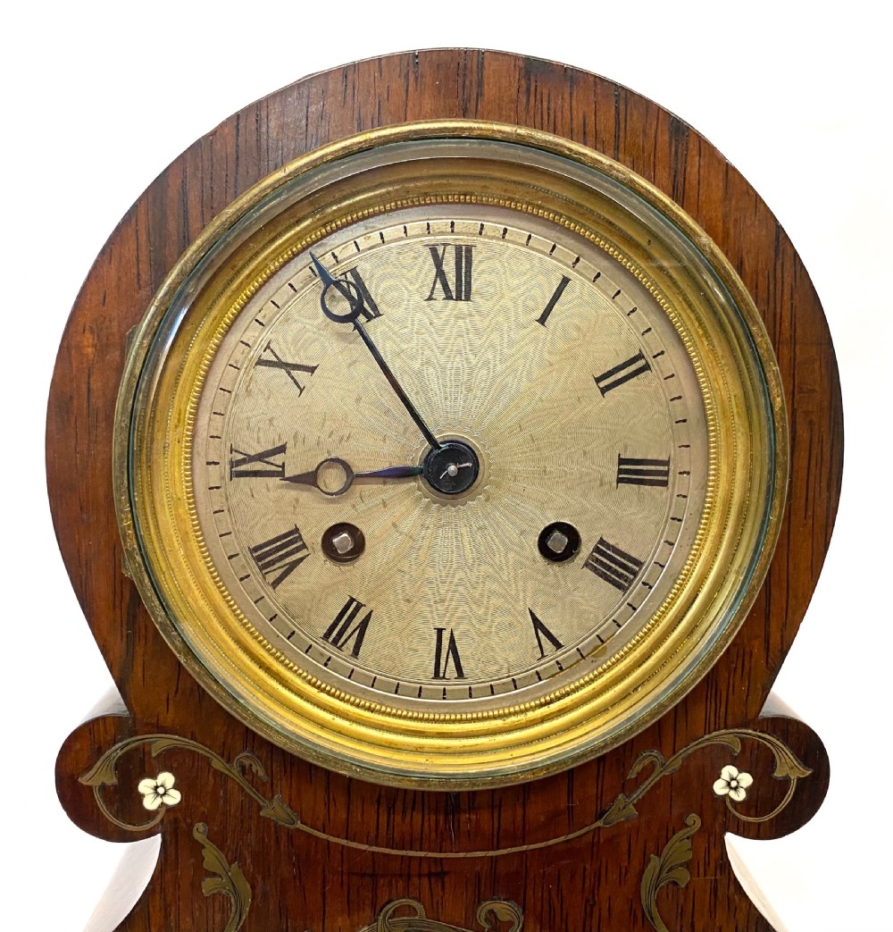 An antique French rosewood mantel clock featuring detailed brass foliage marquetry, bone cherub inlay, and a circular Roman numeral dial. View IV