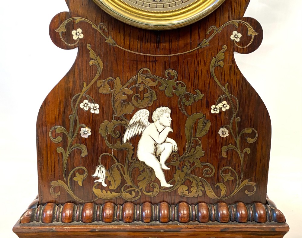 An antique French rosewood mantel clock featuring detailed brass foliage marquetry, bone cherub inlay, and a circular Roman numeral dial. View V