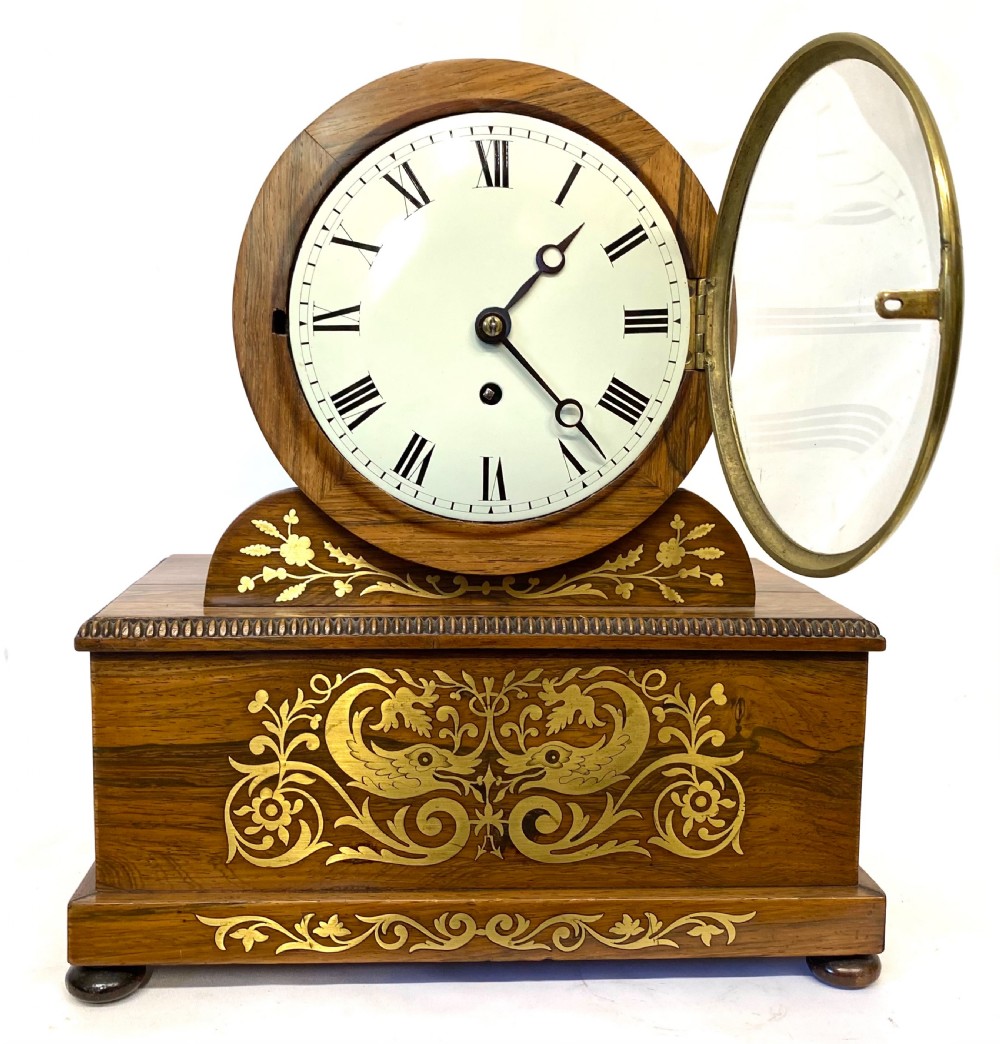 An antique Regency drumhead mantel clock constructed from polished timber with intricate brass floral inlay, a white dial with Roman numerals, and brass ball feet. View II