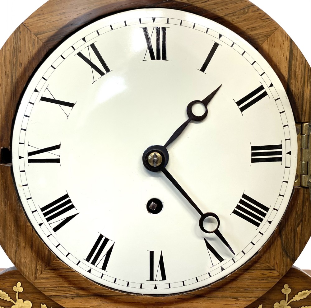 An antique Regency drumhead mantel clock constructed from polished timber with intricate brass floral inlay, a white dial with Roman numerals, and brass ball feet. View III