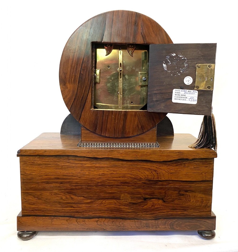An antique Regency drumhead mantel clock constructed from polished timber with intricate brass floral inlay, a white dial with Roman numerals, and brass ball feet. View XII