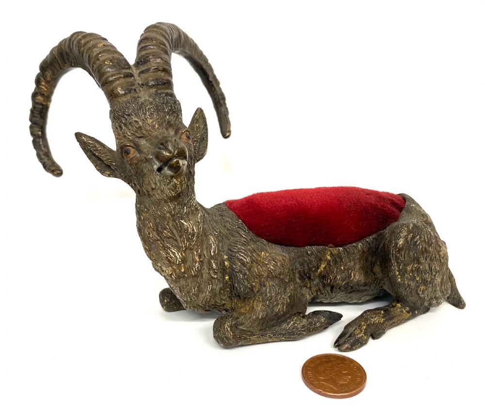 An antique Austrian cold-painted bronze figurine of a recumbent ibex with long curved horns and an integrated red velvet pin cushion set into its back.
