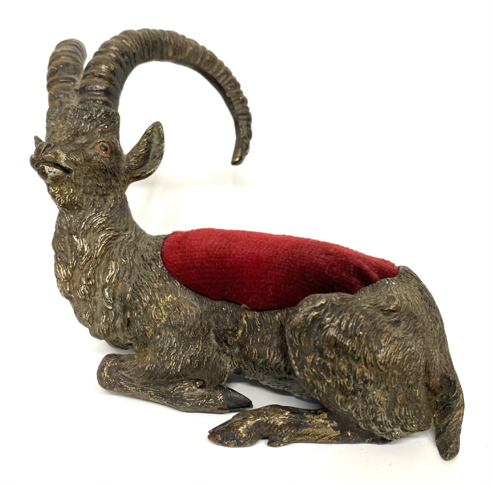 An antique Austrian cold-painted bronze figurine of a recumbent ibex with long curved horns and an integrated red velvet pin cushion set into its back. View II
