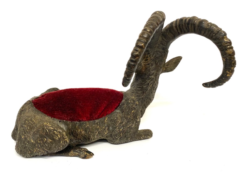 An antique Austrian cold-painted bronze figurine of a recumbent ibex with long curved horns and an integrated red velvet pin cushion set into its back. View V