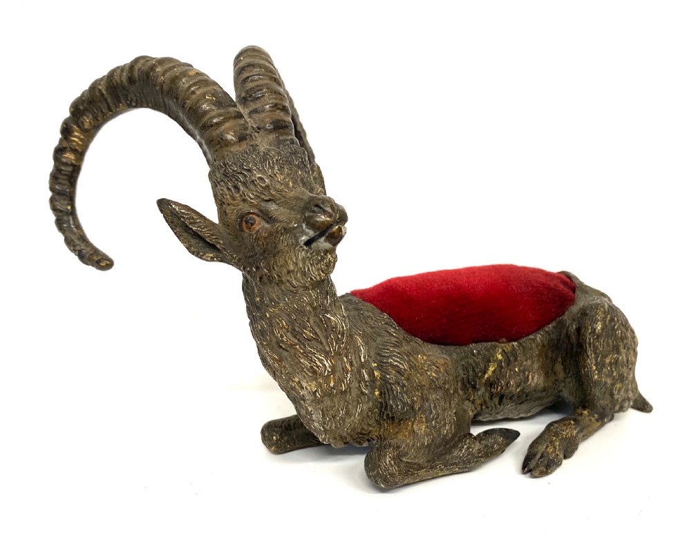 An antique Austrian cold-painted bronze figurine of a recumbent ibex with long curved horns and an integrated red velvet pin cushion set into its back. View VIII
