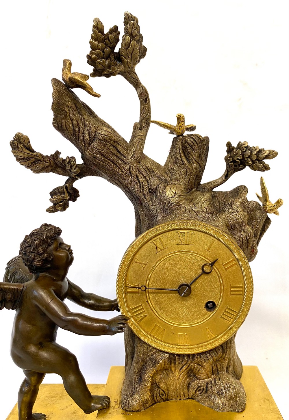 An antique gilt and patinated bronze mantel clock featuring a dark bronze cherub beside a tree stump clock housing topped with small birds. View III