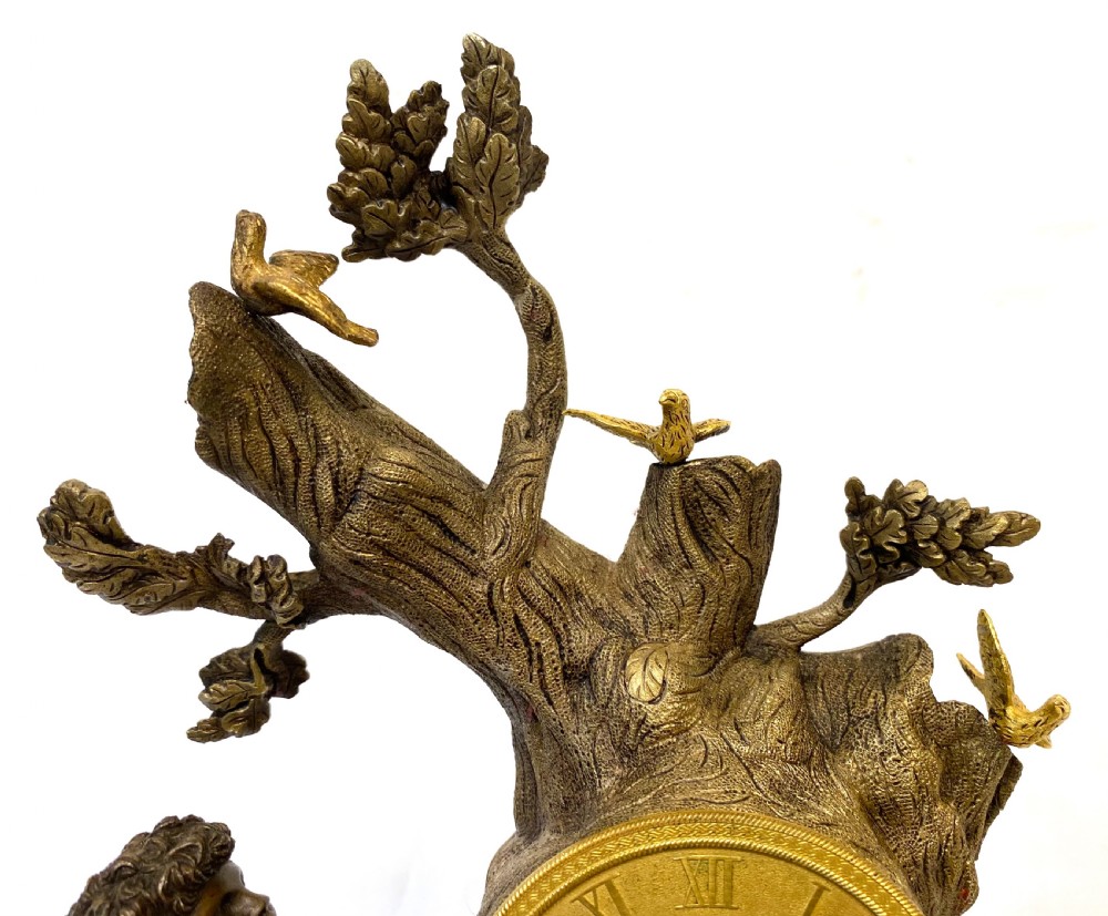 An antique gilt and patinated bronze mantel clock featuring a dark bronze cherub beside a tree stump clock housing topped with small birds. View V