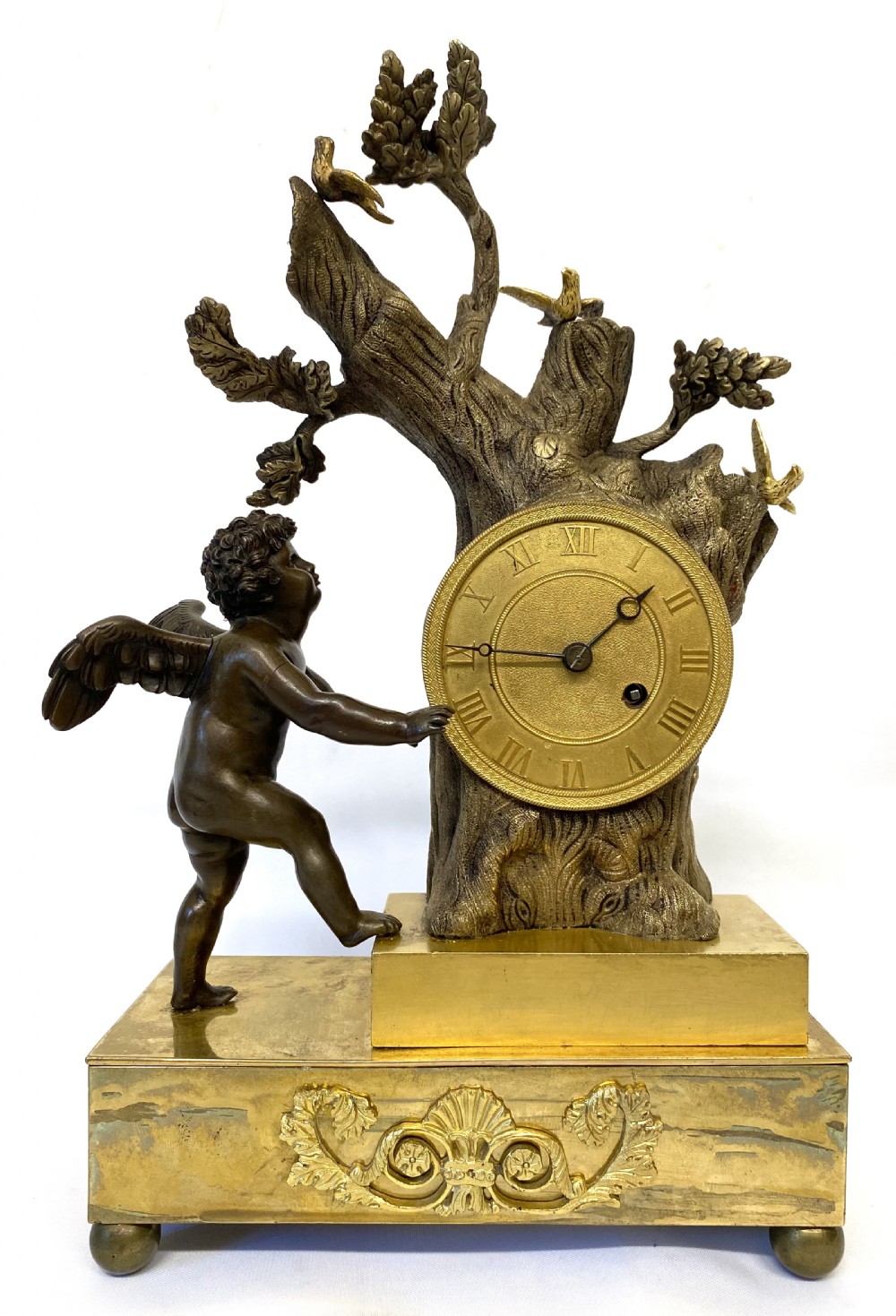 An antique gilt and patinated bronze mantel clock featuring a dark bronze cherub beside a tree stump clock housing topped with small birds. View X