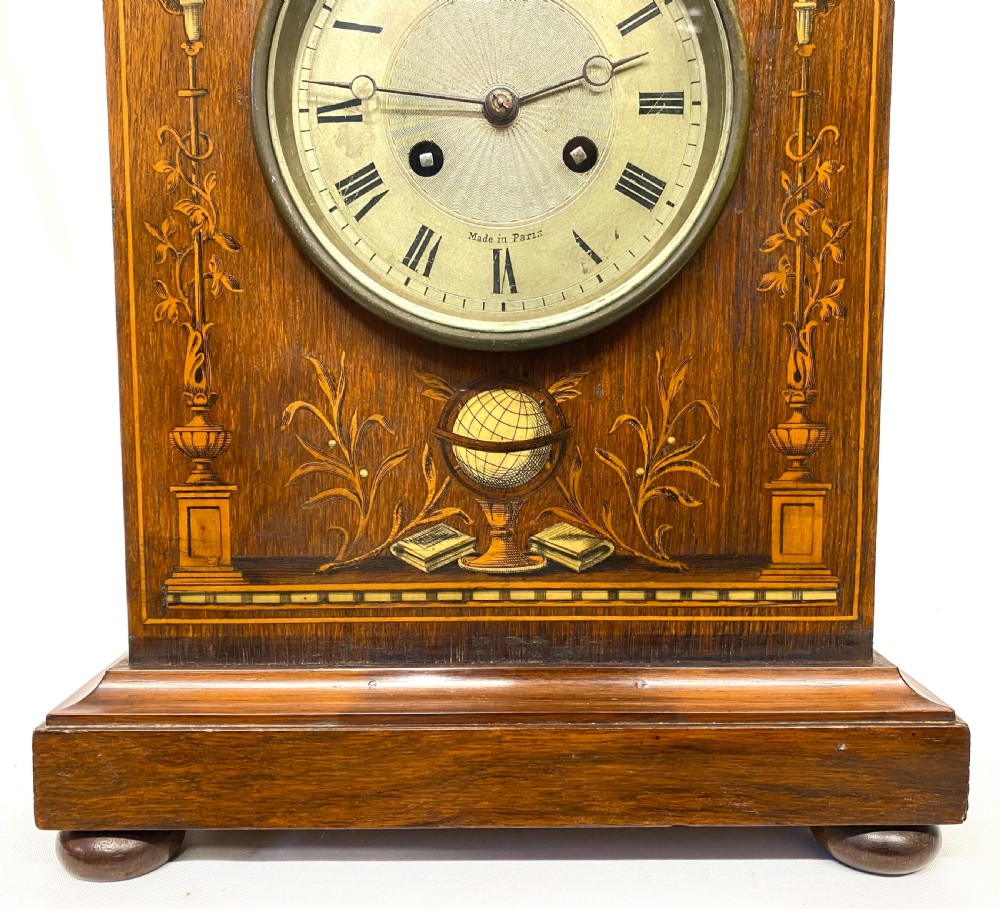 An antique rosewood mantel clock featuring intricate marquetry inlays of figures, swags, and a globe surrounding a circular dial with Roman numerals. View IV