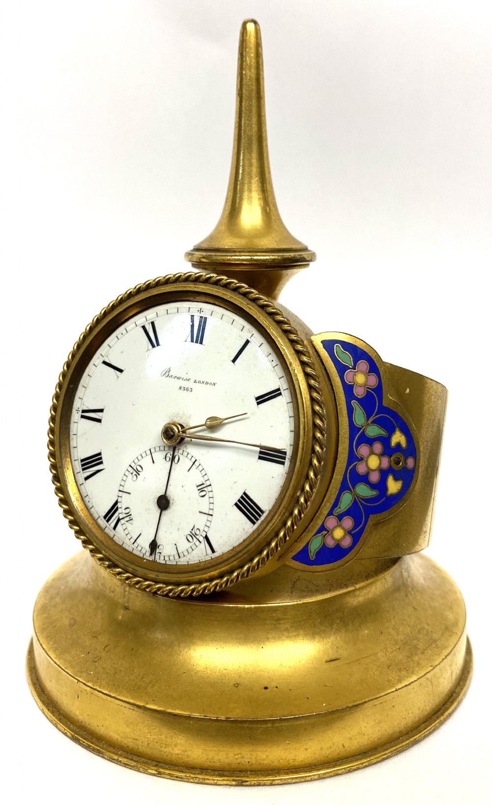 An antique gilt bronze desk clock featuring a white enamel dial with Roman numerals, flanked by blue floral champleve enamel wings and topped with a tapered finial.