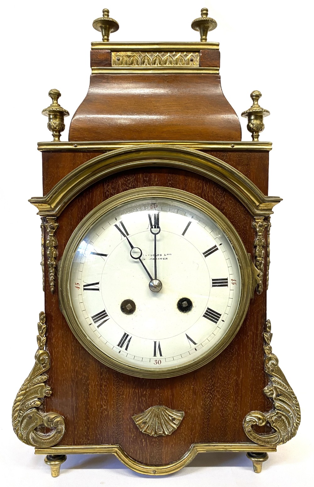 A French mahogany mantel clock featuring ornate gilt ormolu mounts, brass finials, and a white circular dial with Roman numerals.