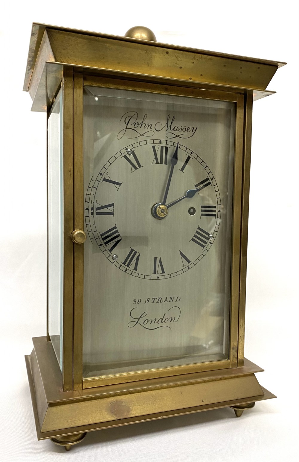 An antique brass four-glass library clock featuring an engraved silvered dial with Roman numerals and glass side panels.