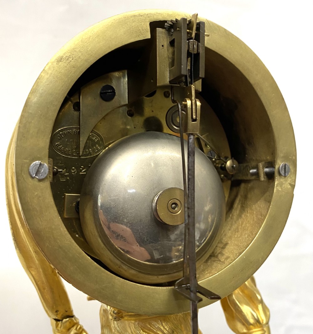 A gilt bronze Victorian mantel clock featuring a sculpted cherub supporting a circular white enamel clock dial signed John Bennett London. View IX