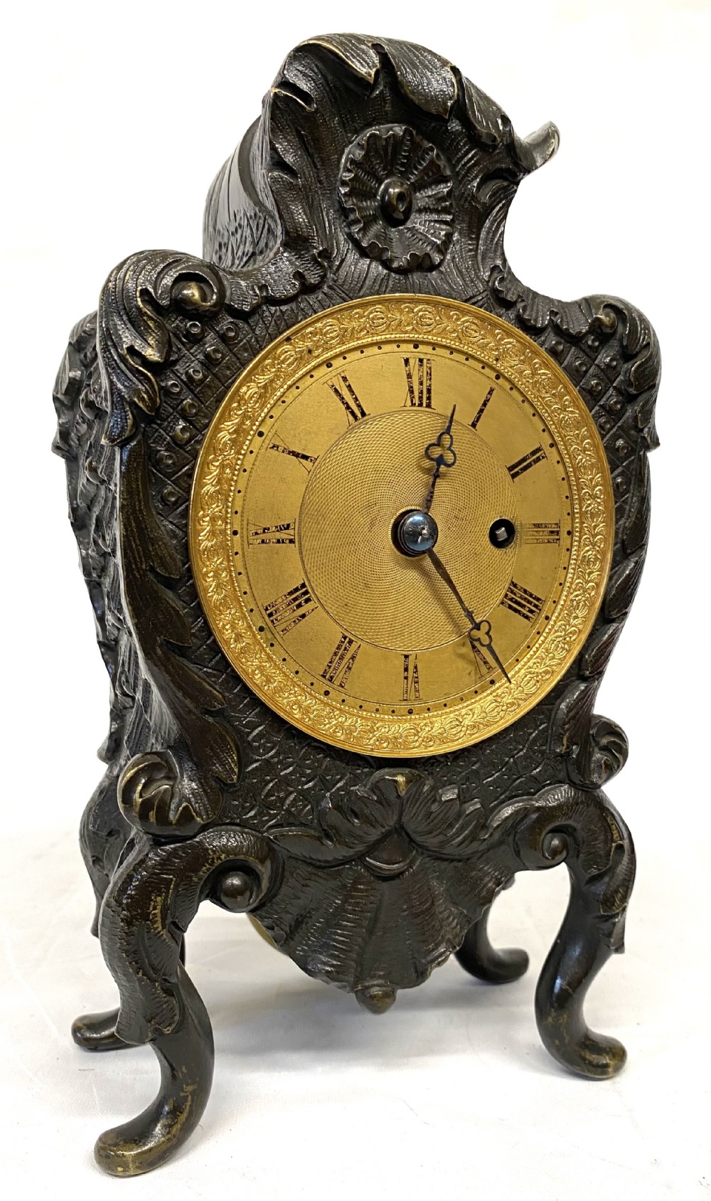 An antique miniature bronze mantel clock featuring Rococo scrollwork, cabriole legs, and an engraved gold-tone brass dial with Roman numerals.