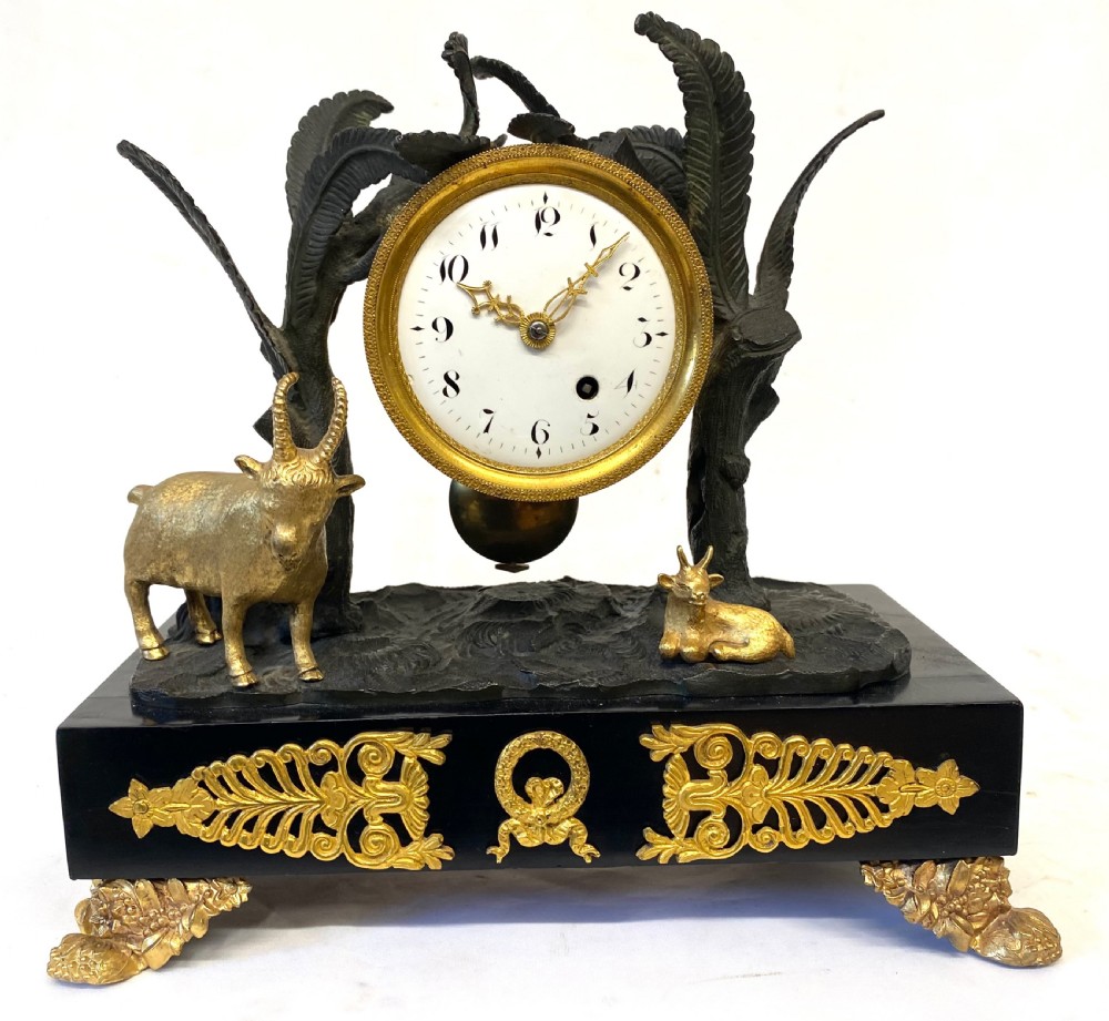 An antique Regency gilt and patinated bronze mantel clock featuring sculpted goats beneath palm trees on a black rectangular base with scrolled gilt feet. View IV