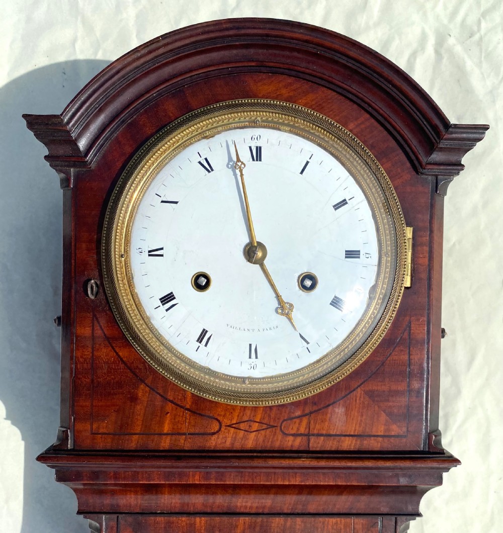 An antique flame mahogany wall clock featuring a round white enamel dial, brass bezel, and a glazed door displaying a gridiron pendulum. View III