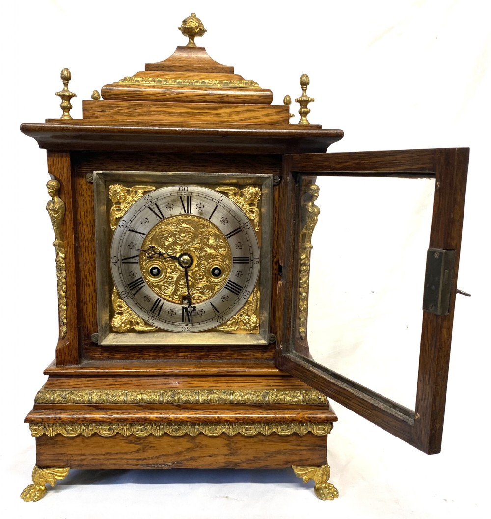 An antique oak double fusee mantel clock with brass caryatid corner mounts, brass finials, an engraved metal dial with Roman numerals, and brass bracket feet. View II