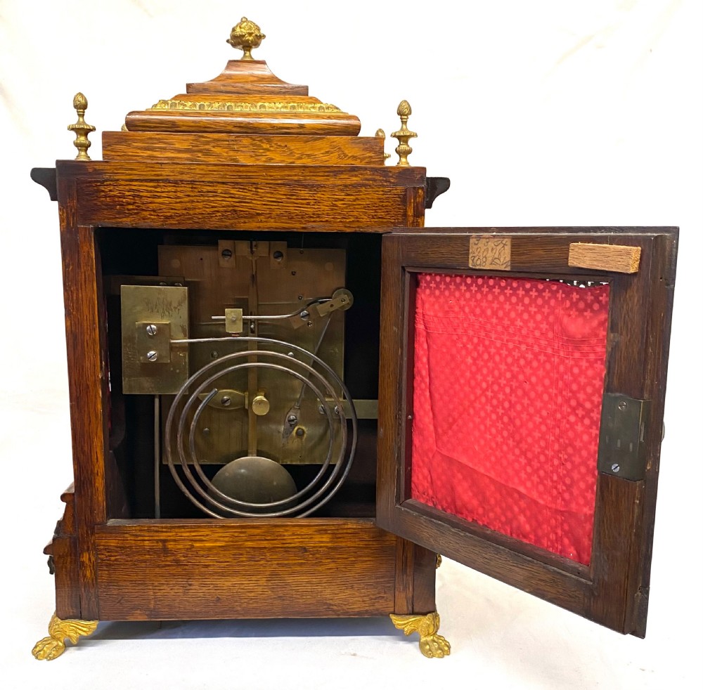 An antique oak double fusee mantel clock with brass caryatid corner mounts, brass finials, an engraved metal dial with Roman numerals, and brass bracket feet. View VIII