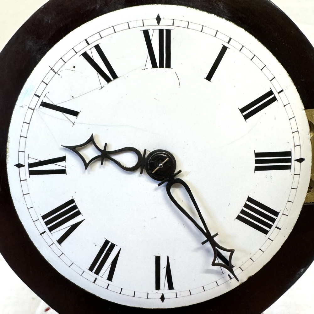 A dark mahogany miniature balloon clock featuring a circular white enamel dial with Roman numerals, a brass acorn finial, and brass feet. View V