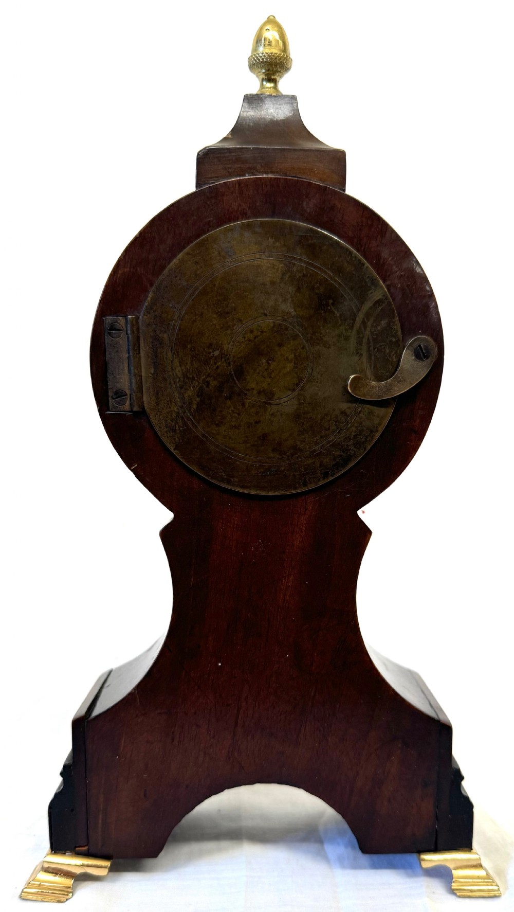 A dark mahogany miniature balloon clock featuring a circular white enamel dial with Roman numerals, a brass acorn finial, and brass feet. View VIII