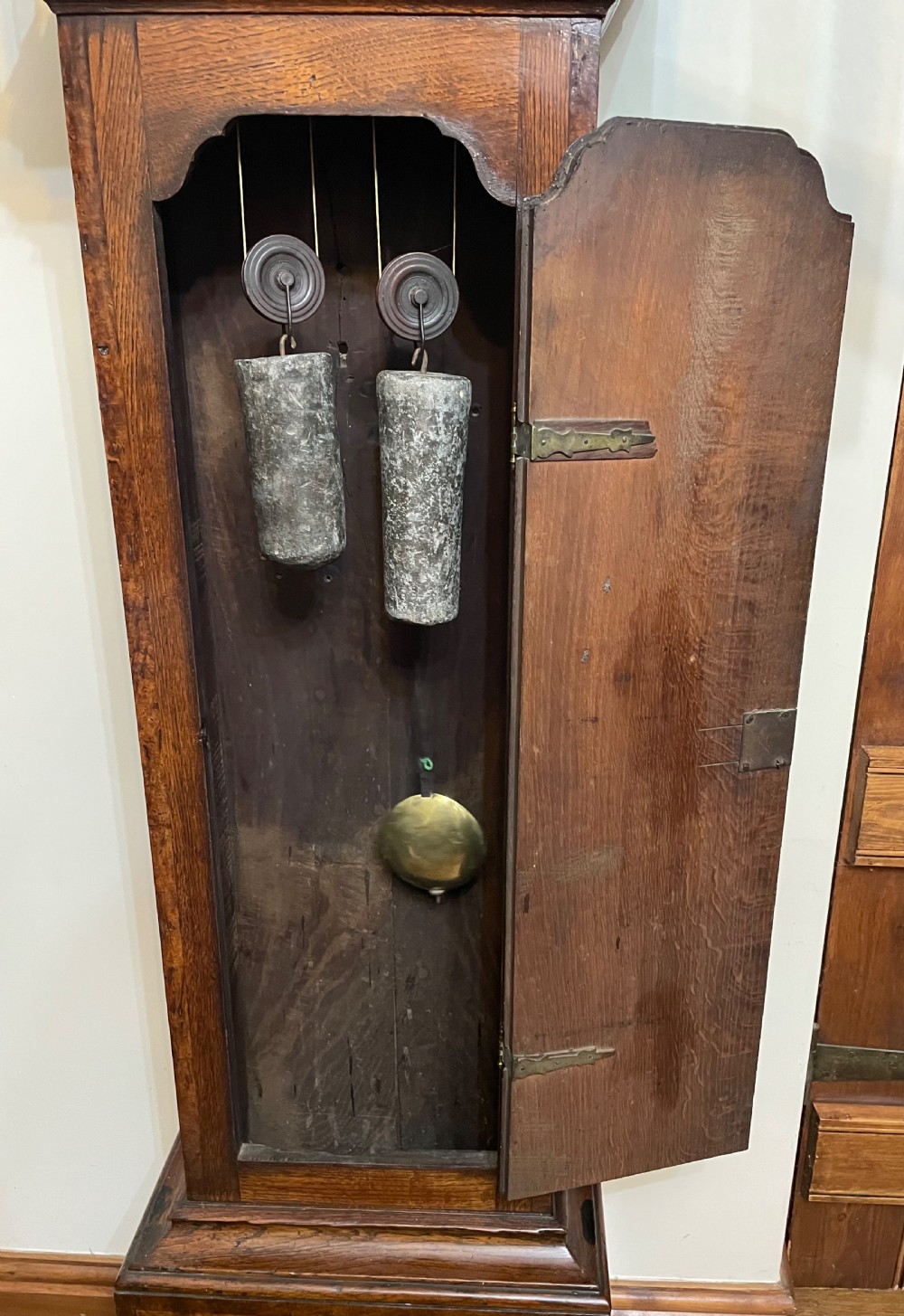 An antique dark oak longcase grandfather clock featuring a carved wooden hood, brass dial with Roman numerals, and a tall rectangular trunk door. View XIII