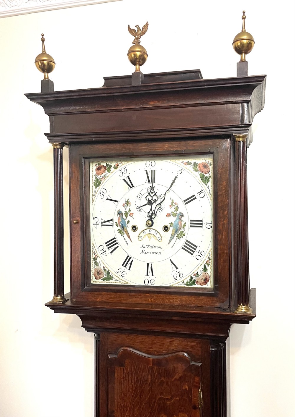 An antique oak and mahogany longcase grandfather clock featuring three brass ball finials, a hand-painted dial face, and fluted column details. View III