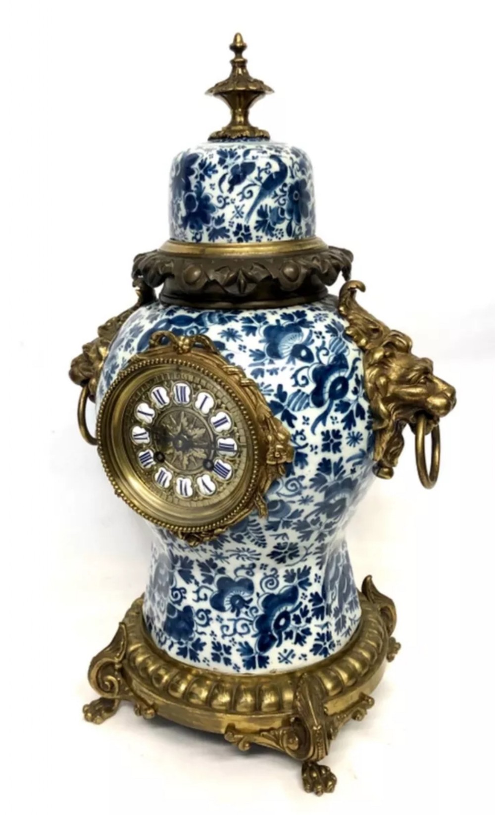 A porcelain urn-shaped mantel clock decorated with blue and white floral patterns, featuring gilt bronze lion mask side handles and a cast metal scrolled base.