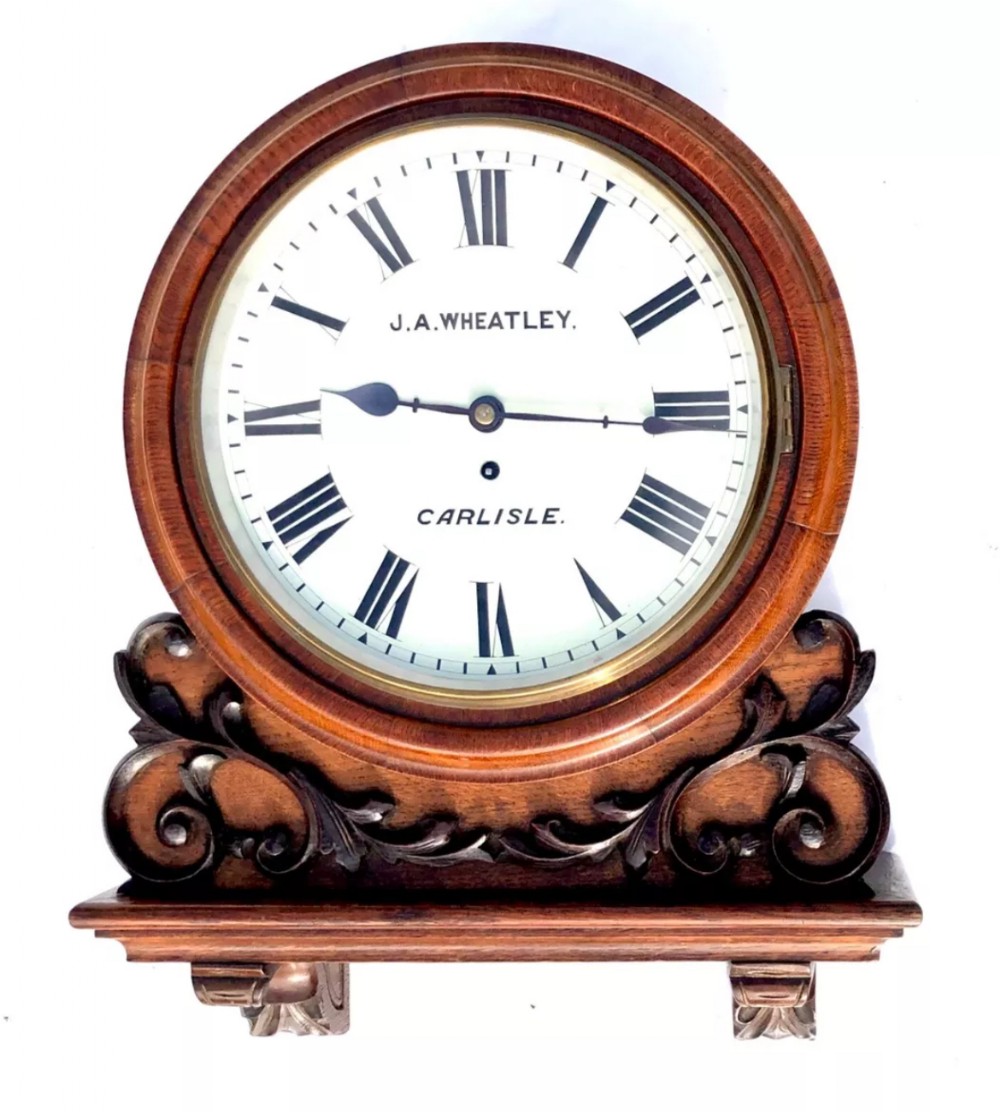 Victorian mahogany circular fusee wall clock with carved scrollwork base and a white dial signed J. A. Wheatley Carlisle.