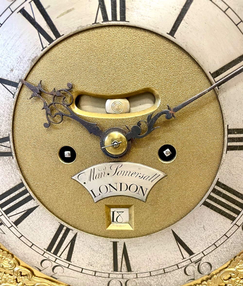An 18th-century ebonised wooden bracket clock featuring a brass dial with silvered chapter rings, decorative corner spandrels, a strike/silent sub-dial, and a brass carrying handle on top. View VIII