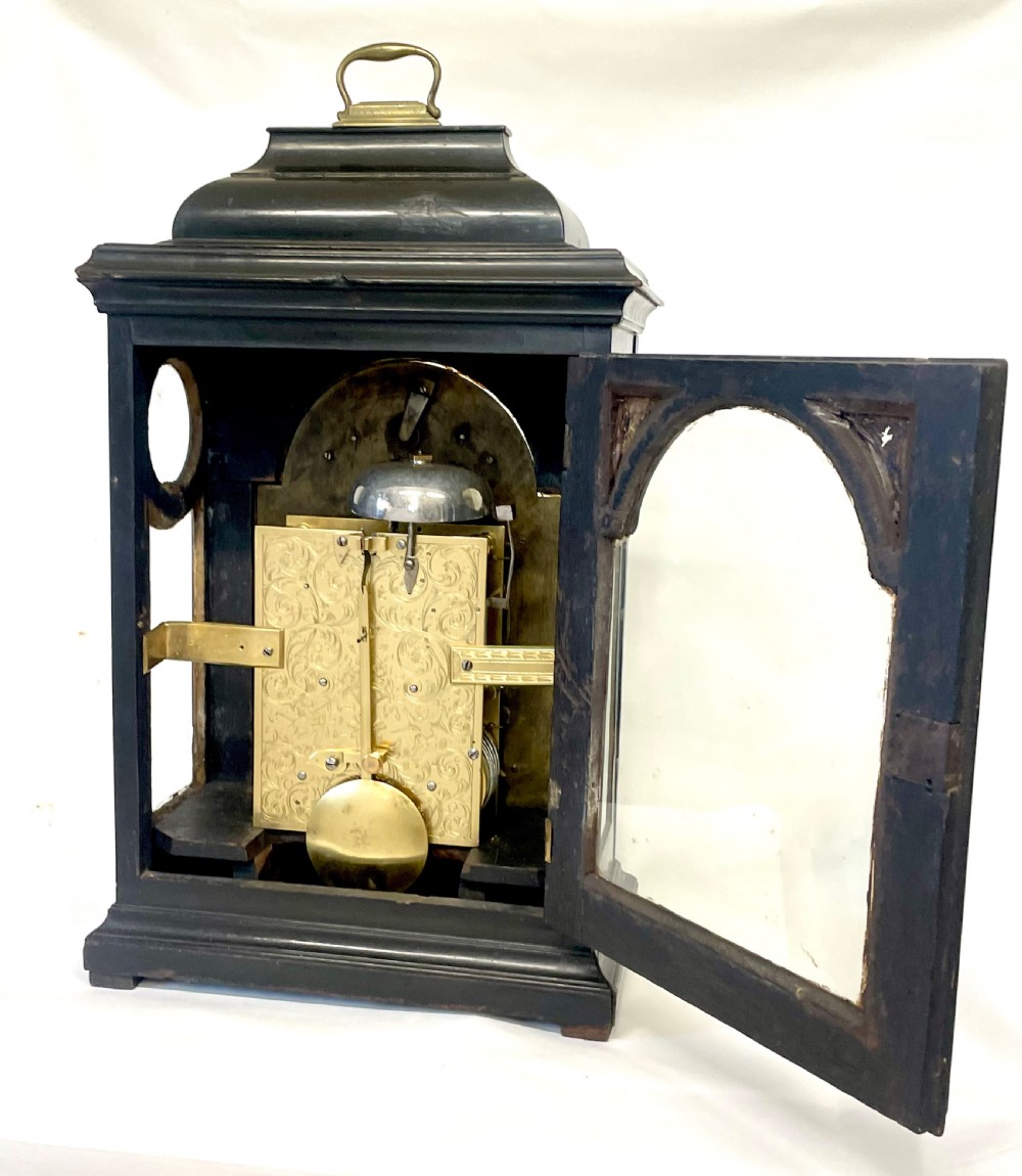 An 18th-century ebonised wooden bracket clock featuring a brass dial with silvered chapter rings, decorative corner spandrels, a strike/silent sub-dial, and a brass carrying handle on top. View XV