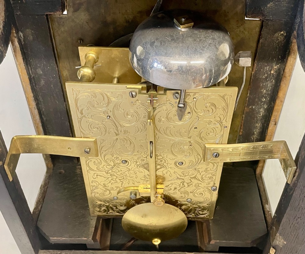 An 18th-century ebonised wooden bracket clock featuring a brass dial with silvered chapter rings, decorative corner spandrels, a strike/silent sub-dial, and a brass carrying handle on top. View XVI