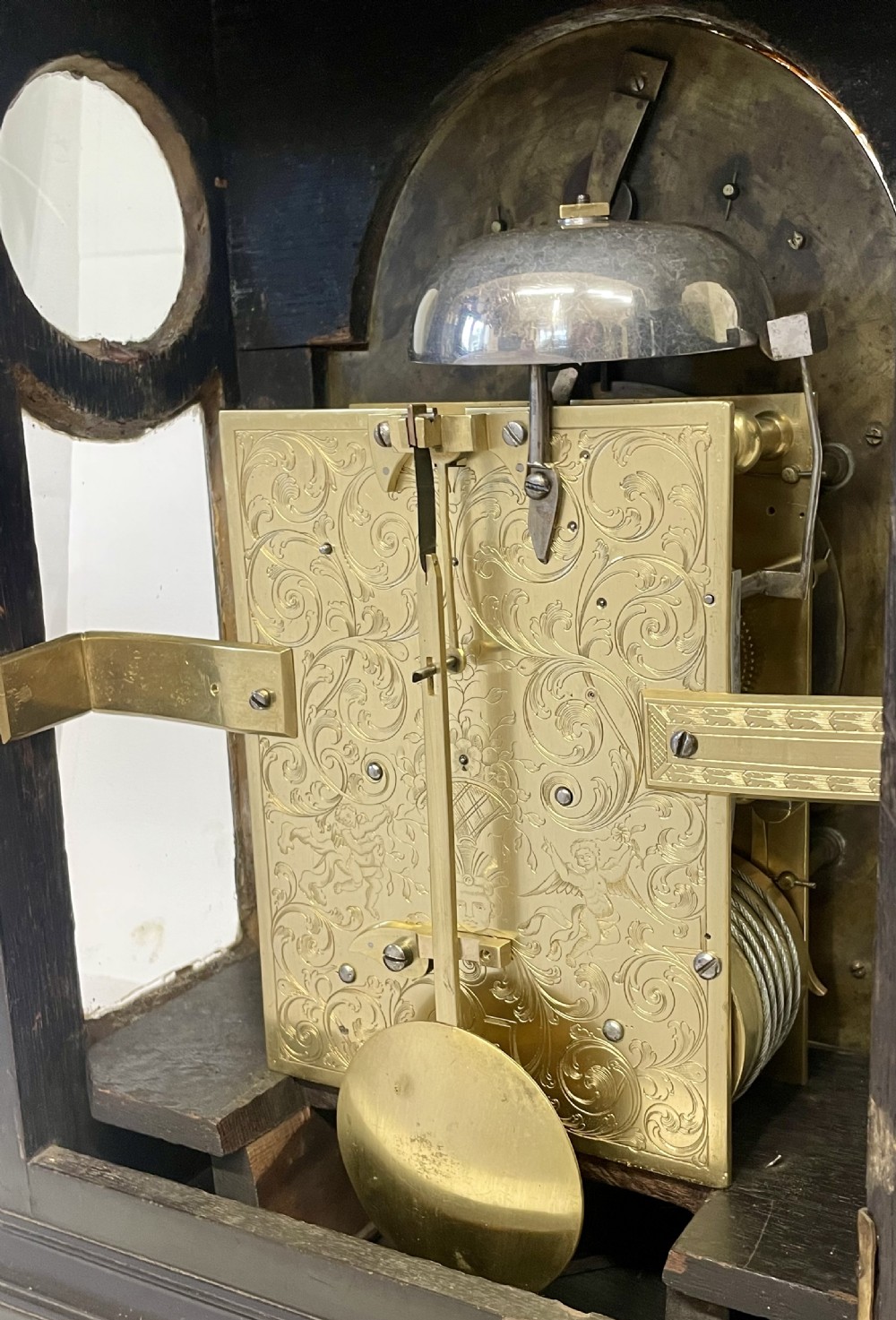An 18th-century ebonised wooden bracket clock featuring a brass dial with silvered chapter rings, decorative corner spandrels, a strike/silent sub-dial, and a brass carrying handle on top. View XVII