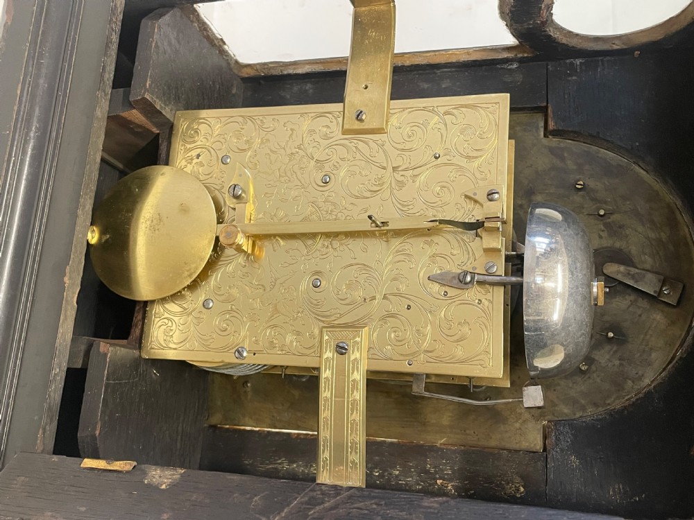An 18th-century ebonised wooden bracket clock featuring a brass dial with silvered chapter rings, decorative corner spandrels, a strike/silent sub-dial, and a brass carrying handle on top. View XVIII