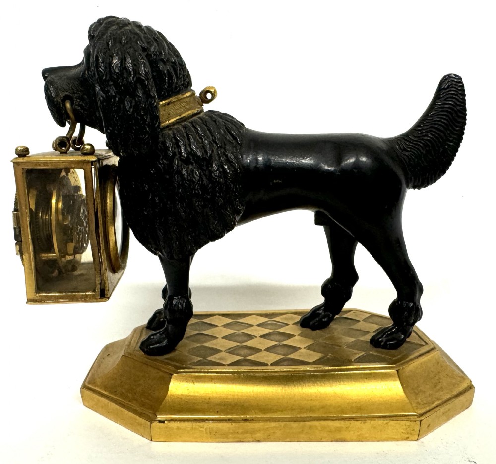A French gilt and patinated bronze timepiece featuring a standing dog figure holding a square glass clock case in its mouth on a gilded base. View IX