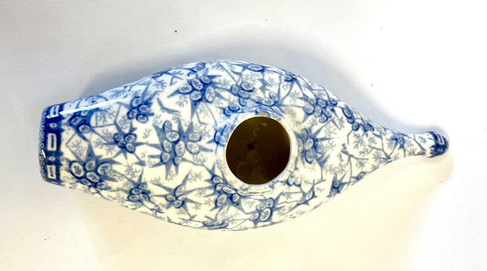 A nineteenth-century ceramic baby feeding bottle decorated with blue and white floral transferware motifs, featuring a central circular opening and an elongated spout. View VIII