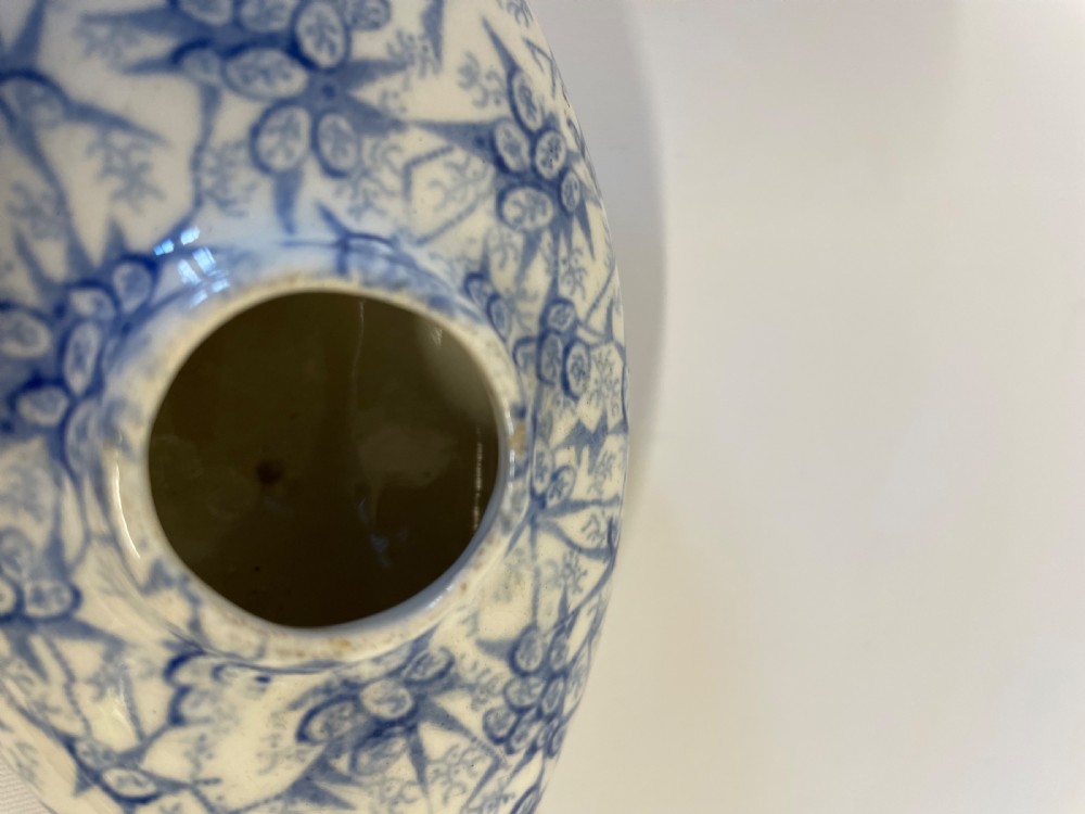 A nineteenth-century ceramic baby feeding bottle decorated with blue and white floral transferware motifs, featuring a central circular opening and an elongated spout. View XI