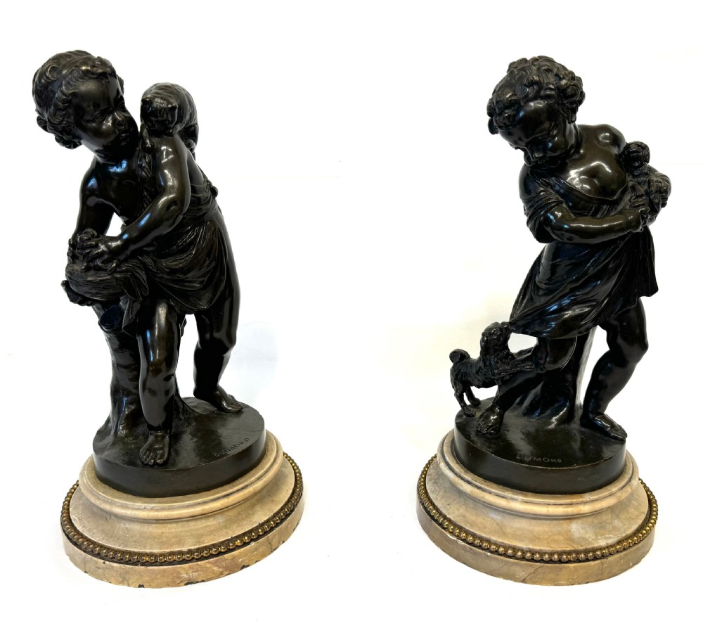 A pair of patinated dark bronze sculptures of children playing with animals, mounted on circular marble bases.