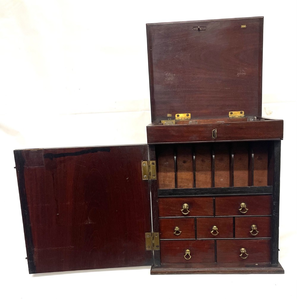 A Georgian dark mahogany apothecary chest with an open hinged lid revealing glass stoppered bottles, a side-hinged door, and interior drawers with brass handles. View II