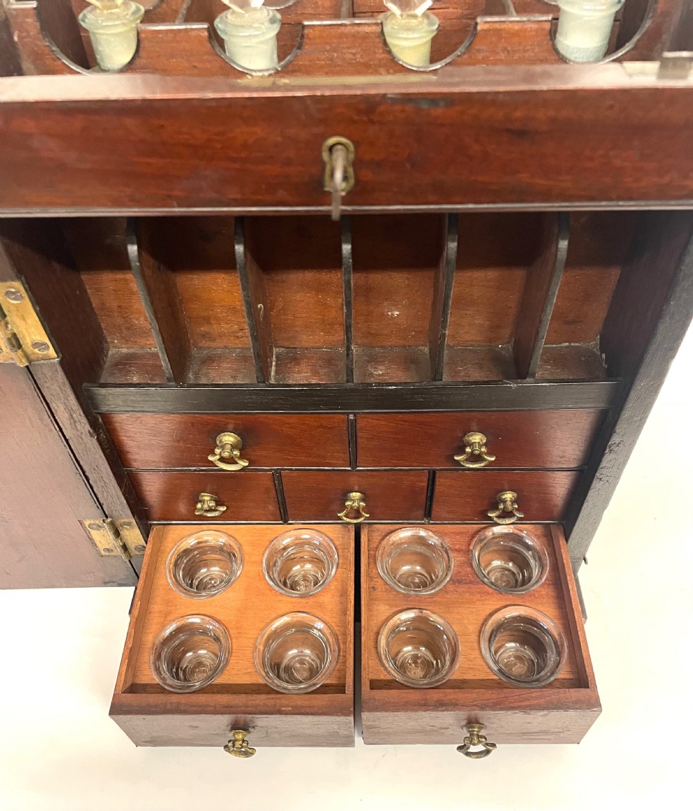 A Georgian dark mahogany apothecary chest with an open hinged lid revealing glass stoppered bottles, a side-hinged door, and interior drawers with brass handles. View IX