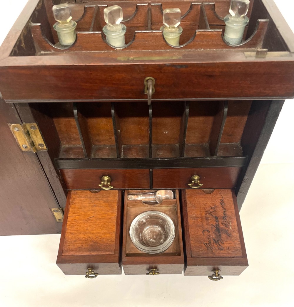 A Georgian dark mahogany apothecary chest with an open hinged lid revealing glass stoppered bottles, a side-hinged door, and interior drawers with brass handles. View X