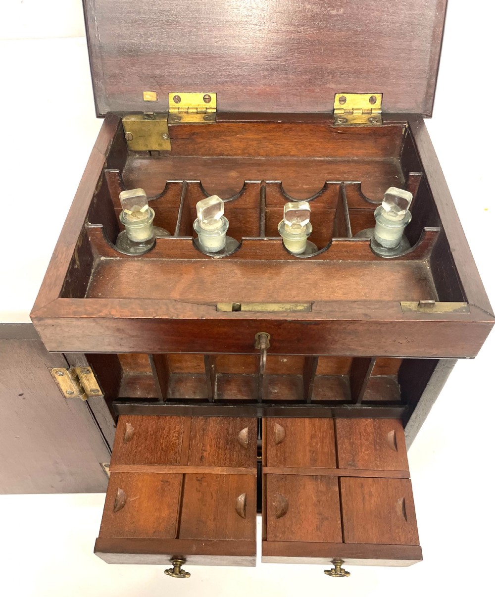 A Georgian dark mahogany apothecary chest with an open hinged lid revealing glass stoppered bottles, a side-hinged door, and interior drawers with brass handles. View XI
