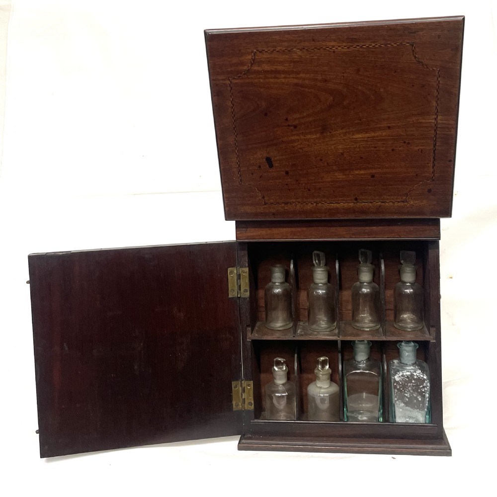 A Georgian dark mahogany apothecary chest with an open hinged lid revealing glass stoppered bottles, a side-hinged door, and interior drawers with brass handles. View XV