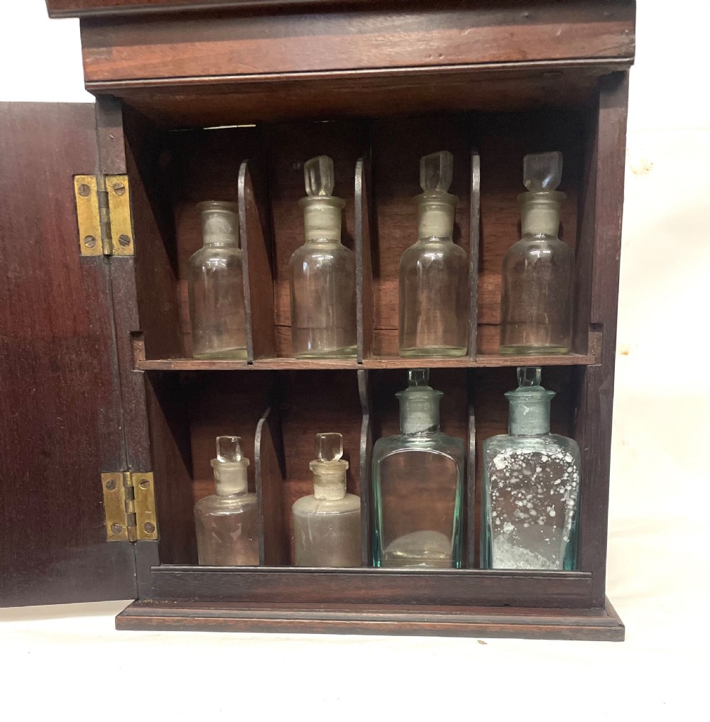 A Georgian dark mahogany apothecary chest with an open hinged lid revealing glass stoppered bottles, a side-hinged door, and interior drawers with brass handles. View XVI