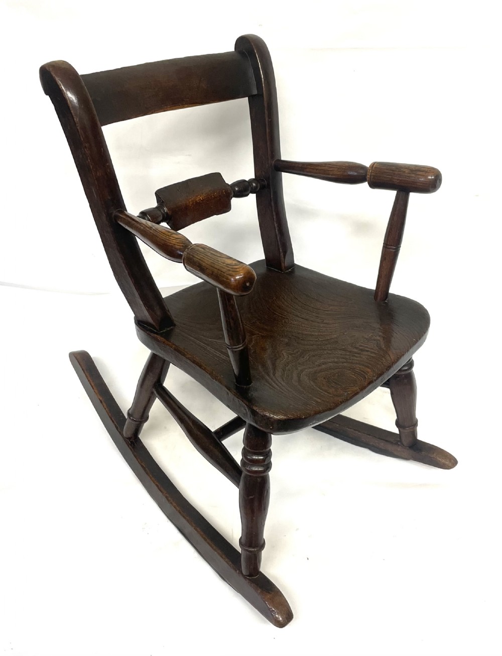 A dark brown wooden childs or dolls rocking armchair featuring turned legs, curved armrests, and smooth wooden rockers.