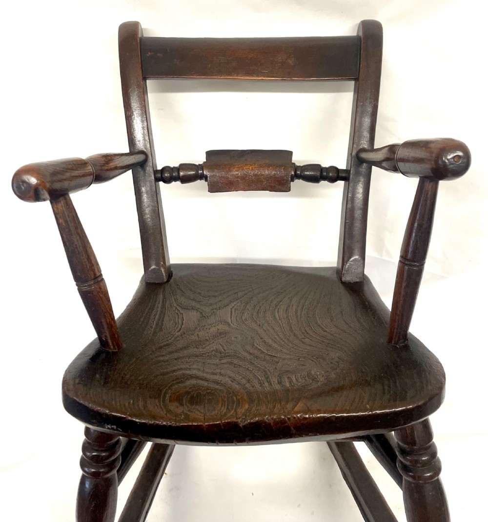 A dark brown wooden childs or dolls rocking armchair featuring turned legs, curved armrests, and smooth wooden rockers. View IV
